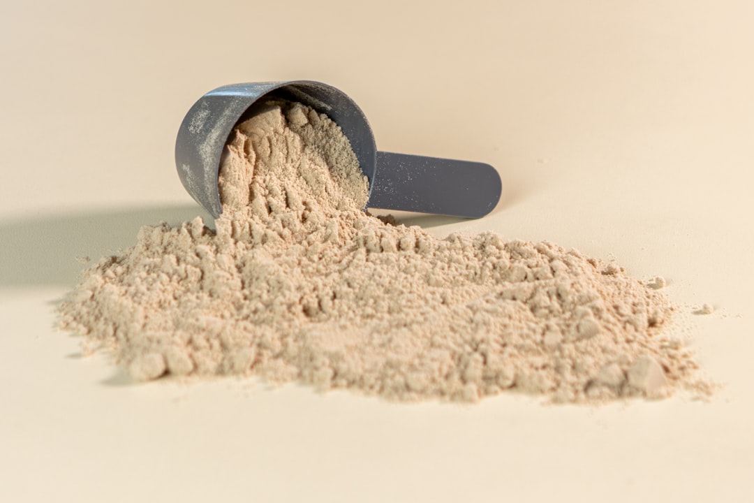 A variety of protein powder containers with measuring scoops and ingredients like fruits and nuts on a wooden table.