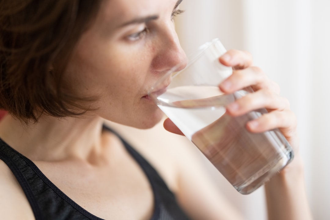 A person drinking water during a workout, with a water bottle and a towel nearby, set in a gym or outdoor environment.